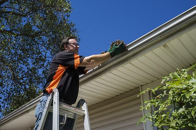 worker repairing a damaged gutter on a residential roof in Kensington CT